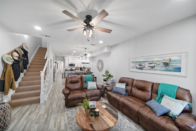 living room with ceiling fan with notable chandelier and light hardwood / wood-style floors