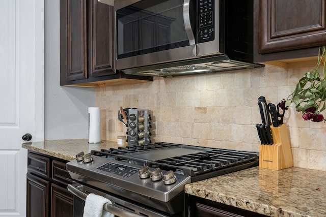 kitchen with dark brown cabinetry, stainless steel appliances, backsplash, and light stone counters