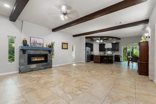 living room with ceiling fan with notable chandelier, a tiled fireplace, and beam ceiling