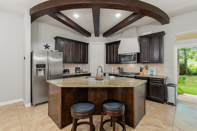 kitchen with beam ceiling, sink, tasteful backsplash, a kitchen island with sink, and appliances with stainless steel finishes