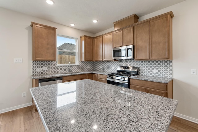 kitchen featuring sink, backsplash, stainless steel appliances, light stone counters, and light wood-type flooring