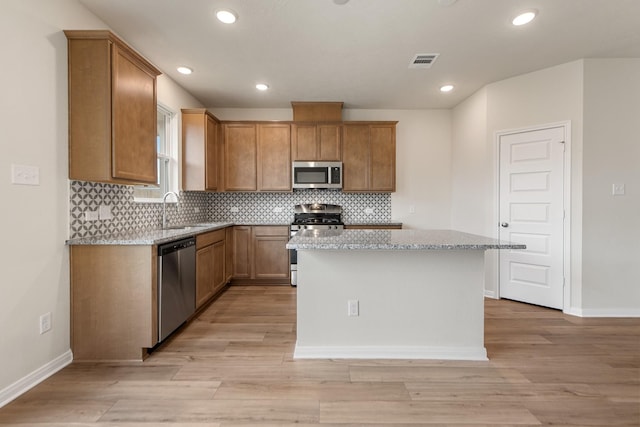 kitchen featuring sink, light hardwood / wood-style flooring, stainless steel appliances, a center island, and light stone counters