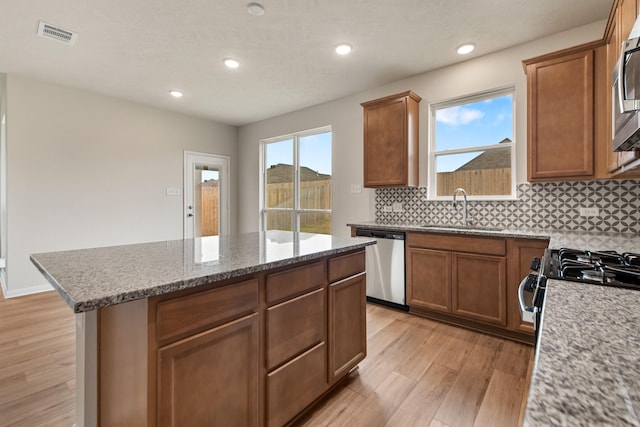 kitchen with a kitchen island, sink, light stone counters, stainless steel appliances, and light hardwood / wood-style flooring