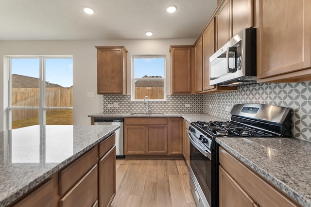 kitchen with sink, backsplash, stainless steel appliances, light stone countertops, and light hardwood / wood-style flooring