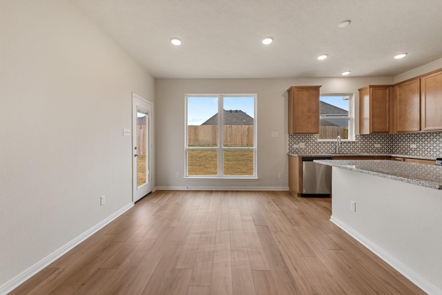 kitchen with sink, decorative backsplash, stainless steel dishwasher, light stone counters, and light hardwood / wood-style floors