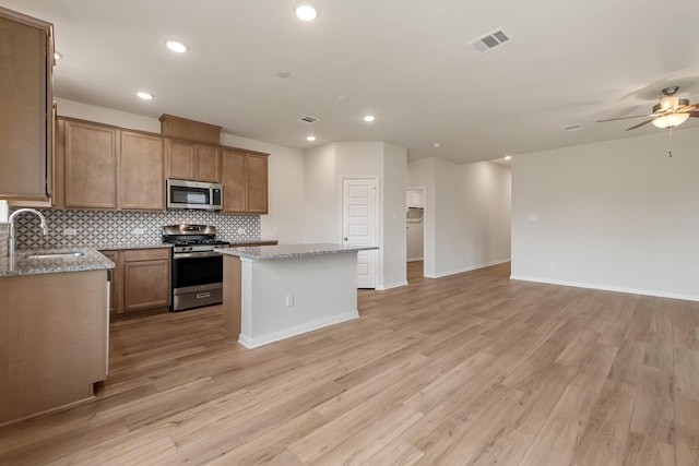 kitchen with sink, light stone counters, tasteful backsplash, a center island, and stainless steel appliances