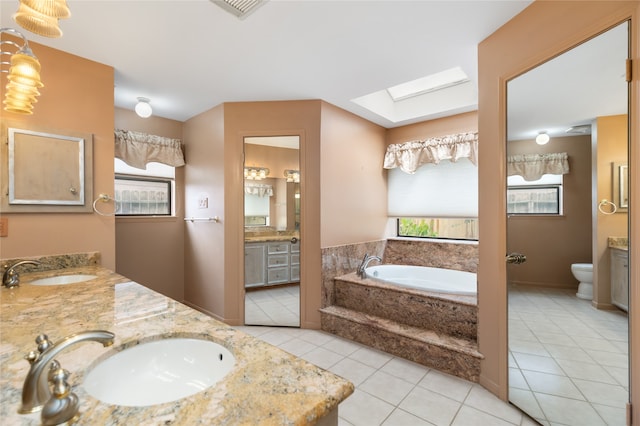 bathroom with tiled bath, vanity, a skylight, toilet, and tile patterned floors