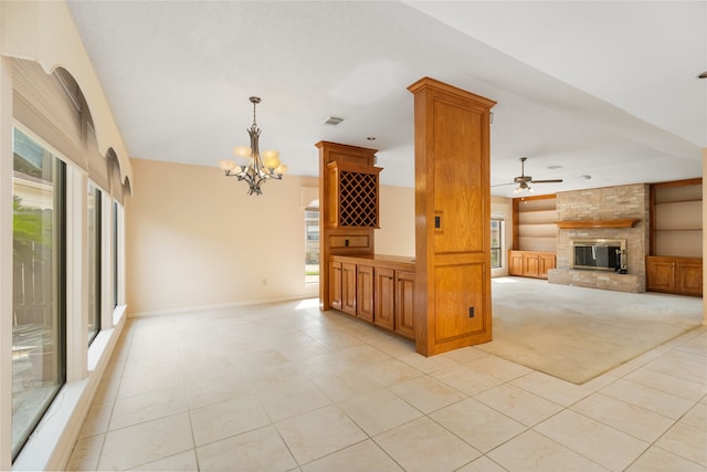 unfurnished living room with ceiling fan with notable chandelier, light tile patterned flooring, and a brick fireplace