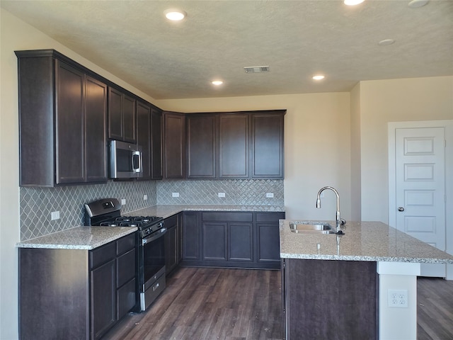 kitchen featuring appliances with stainless steel finishes, light stone counters, dark wood-type flooring, sink, and a center island with sink