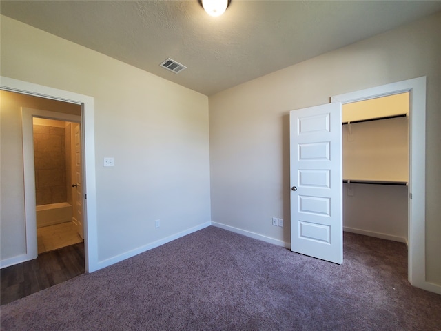 unfurnished bedroom featuring a textured ceiling, a spacious closet, dark carpet, and a closet