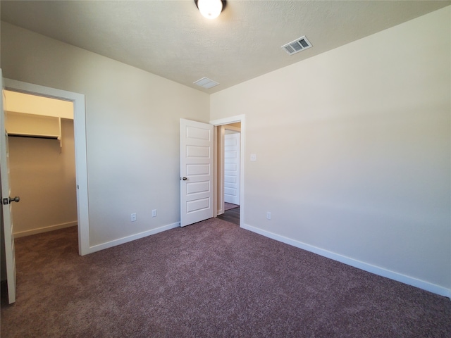 unfurnished bedroom featuring a spacious closet, a closet, and dark colored carpet