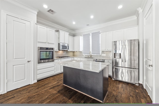 kitchen with light stone counters, white cabinets, dark wood-type flooring, stainless steel appliances, and a center island