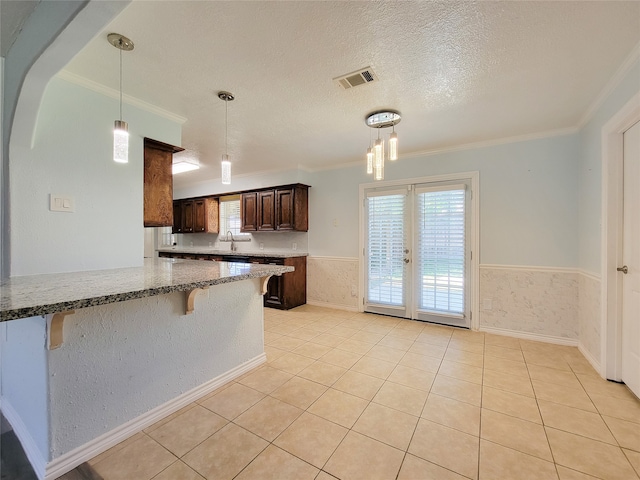 kitchen with light tile patterned floors, kitchen peninsula, a textured ceiling, a breakfast bar, and crown molding