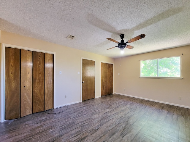 unfurnished bedroom with a textured ceiling, two closets, ceiling fan, and dark hardwood / wood-style flooring