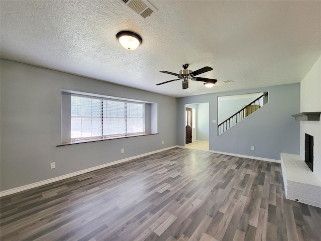 unfurnished living room with ceiling fan, dark hardwood / wood-style floors, a fireplace, and a textured ceiling