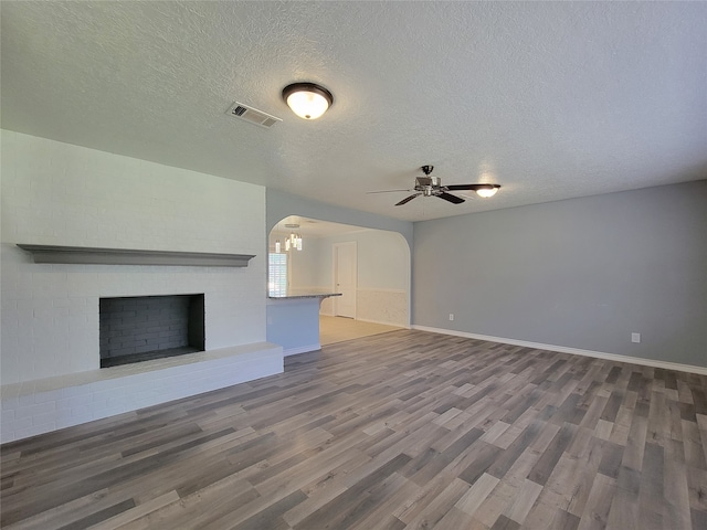 unfurnished living room featuring a textured ceiling, wood-type flooring, a fireplace, and ceiling fan with notable chandelier