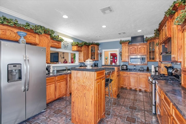 kitchen featuring appliances with stainless steel finishes, a kitchen island, a textured ceiling, ornamental molding, and sink