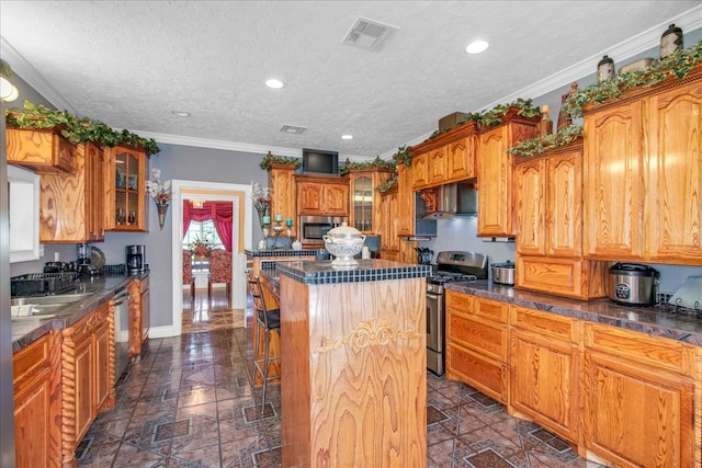 kitchen with appliances with stainless steel finishes, a kitchen island, a textured ceiling, ornamental molding, and wall chimney range hood