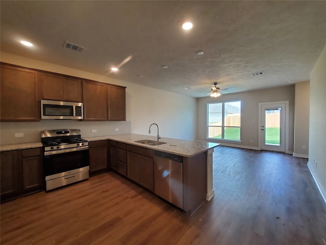 kitchen featuring kitchen peninsula, appliances with stainless steel finishes, dark hardwood / wood-style flooring, light stone counters, and sink