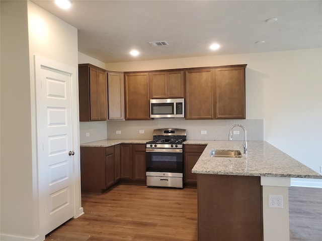 kitchen with kitchen peninsula, light stone countertops, stainless steel appliances, sink, and light hardwood / wood-style flooring