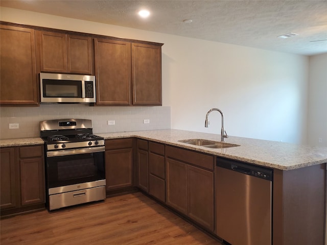 kitchen with kitchen peninsula, light stone counters, stainless steel appliances, dark wood-type flooring, and sink