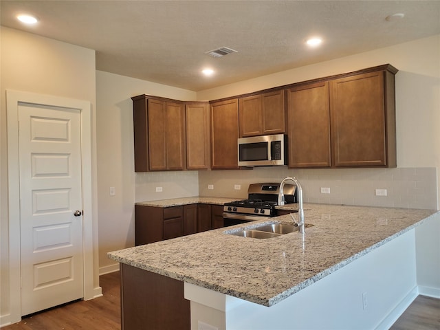 kitchen featuring light stone countertops, appliances with stainless steel finishes, kitchen peninsula, sink, and hardwood / wood-style floors