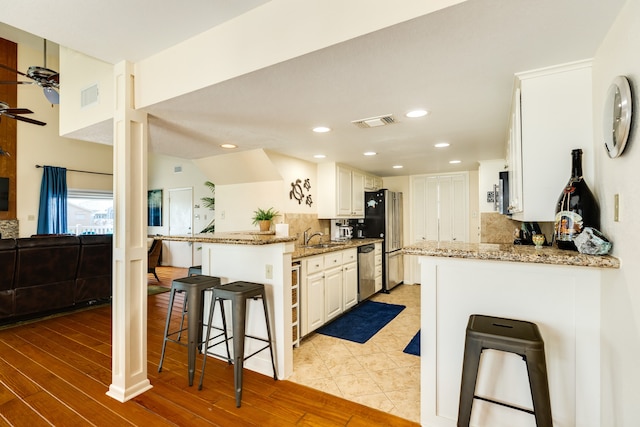 kitchen featuring kitchen peninsula, stone countertops, a kitchen bar, white cabinetry, and light hardwood / wood-style floors