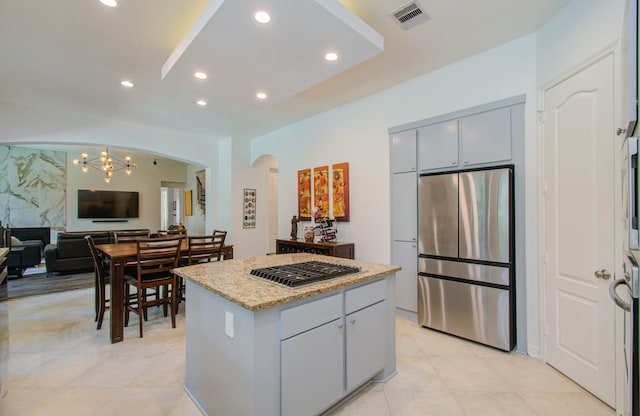 kitchen with light tile patterned flooring, light stone counters, a kitchen island, stainless steel appliances, and an inviting chandelier