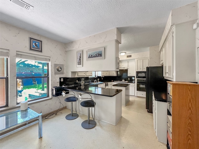 kitchen with kitchen peninsula, a kitchen bar, a textured ceiling, black appliances, and white cabinets