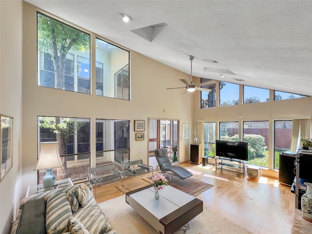 living room featuring ceiling fan, light wood-type flooring, a textured ceiling, and a towering ceiling