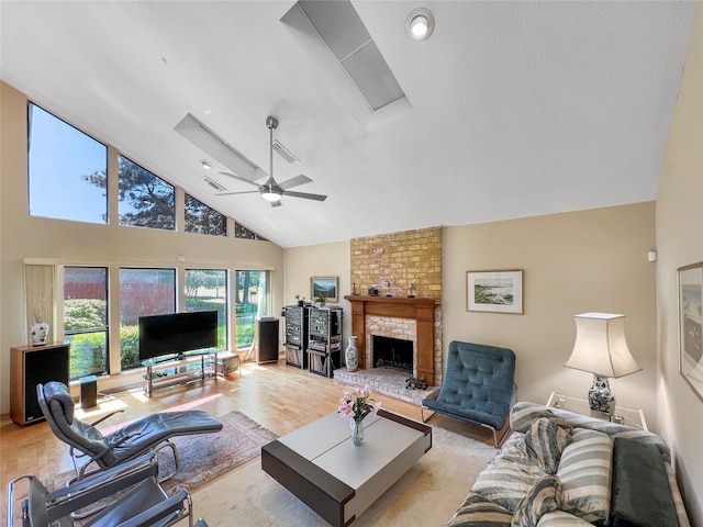 living room featuring high vaulted ceiling, ceiling fan, a textured ceiling, a fireplace, and light hardwood / wood-style floors