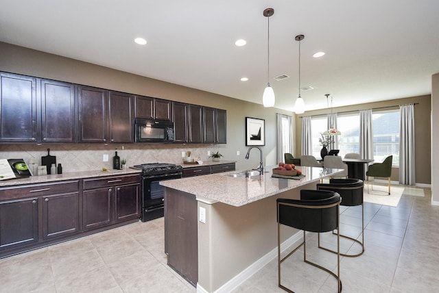 kitchen with black appliances, light stone countertops, hanging light fixtures, a kitchen island with sink, and sink