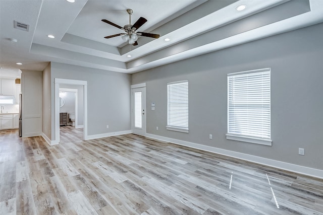 unfurnished living room with light wood-type flooring, ceiling fan, and a raised ceiling