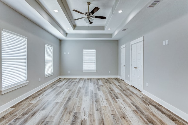 unfurnished room with light hardwood / wood-style flooring, ceiling fan, and a raised ceiling