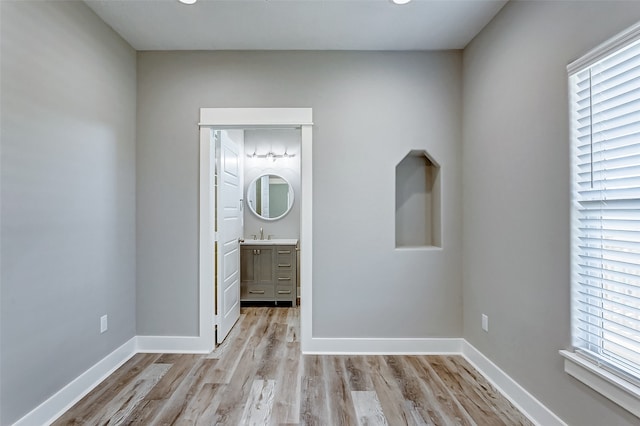 interior space with multiple windows, connected bathroom, light wood-type flooring, and sink