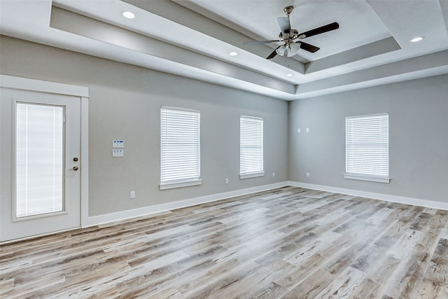 empty room with light hardwood / wood-style floors, a raised ceiling, and ceiling fan