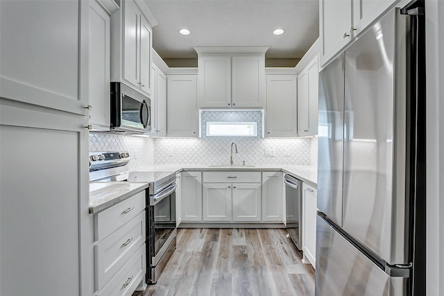 kitchen featuring appliances with stainless steel finishes, light hardwood / wood-style floors, tasteful backsplash, white cabinets, and sink