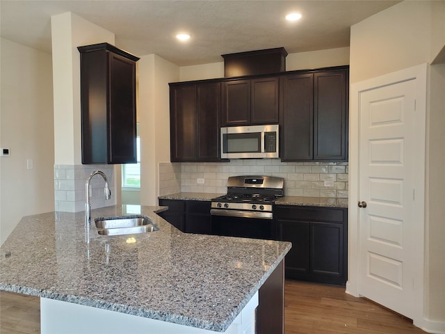 kitchen with sink, stainless steel appliances, tasteful backsplash, light stone counters, and light hardwood / wood-style floors