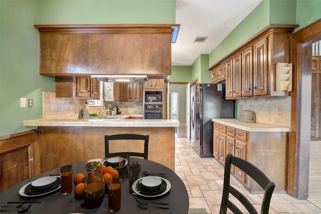 kitchen with tile counters, kitchen peninsula, a textured ceiling, decorative backsplash, and black appliances