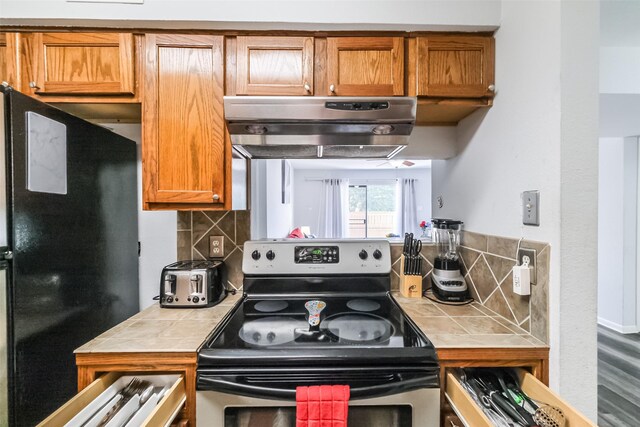 kitchen with black refrigerator, tile countertops, tasteful backsplash, and stainless steel range with electric cooktop