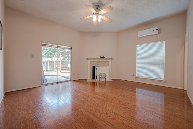 unfurnished living room with a fireplace, an AC wall unit, a textured ceiling, ceiling fan, and hardwood / wood-style floors