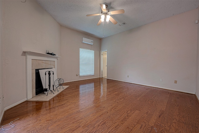 unfurnished living room with a tiled fireplace, a textured ceiling, wood-type flooring, ceiling fan, and a wall mounted AC