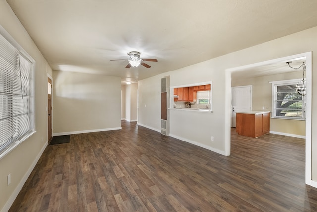 unfurnished living room with ceiling fan with notable chandelier, dark wood-type flooring, and plenty of natural light