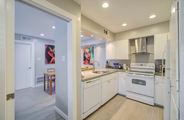 kitchen featuring wall chimney range hood, sink, light wood-type flooring, white cabinets, and white appliances