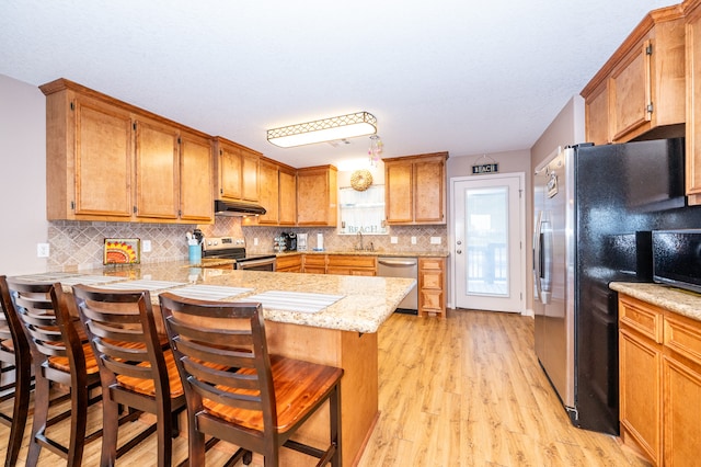 kitchen featuring sink, a breakfast bar area, kitchen peninsula, light hardwood / wood-style flooring, and stainless steel appliances