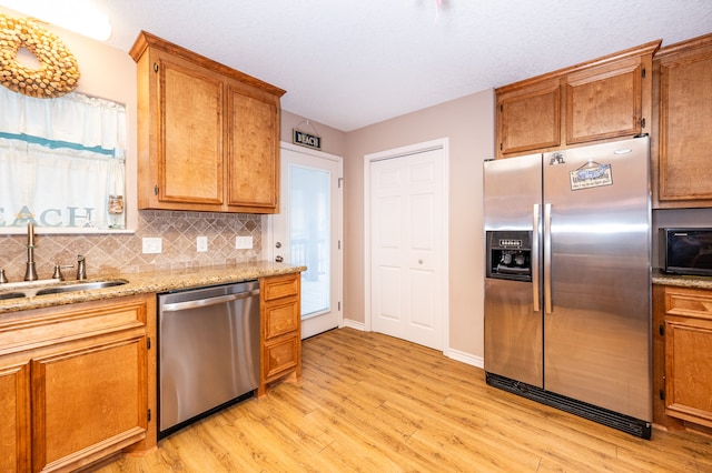 kitchen featuring sink, light hardwood / wood-style flooring, appliances with stainless steel finishes, light stone countertops, and decorative backsplash