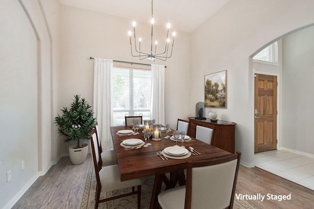 dining space with a towering ceiling, a chandelier, and light wood-type flooring