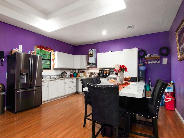 kitchen with light hardwood / wood-style floors, tasteful backsplash, a breakfast bar area, white cabinets, and stainless steel refrigerator with ice dispenser