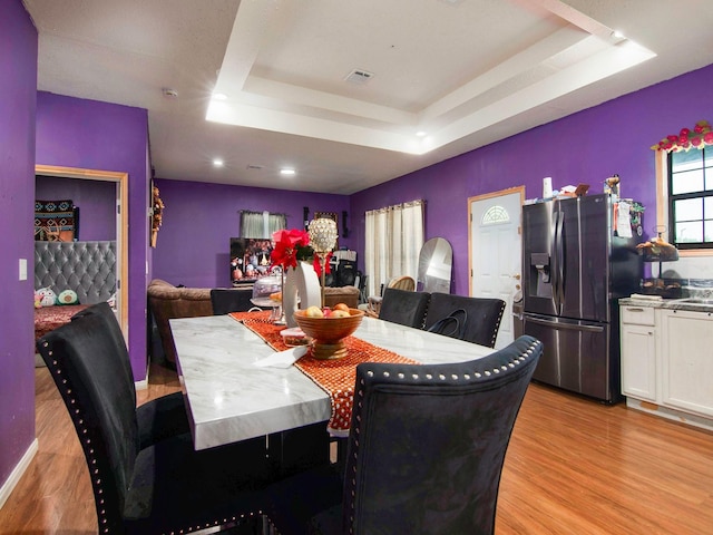 dining space featuring light wood-style flooring, a tray ceiling, and visible vents