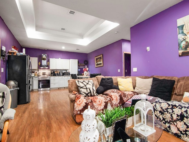 living room with light hardwood / wood-style floors and a tray ceiling